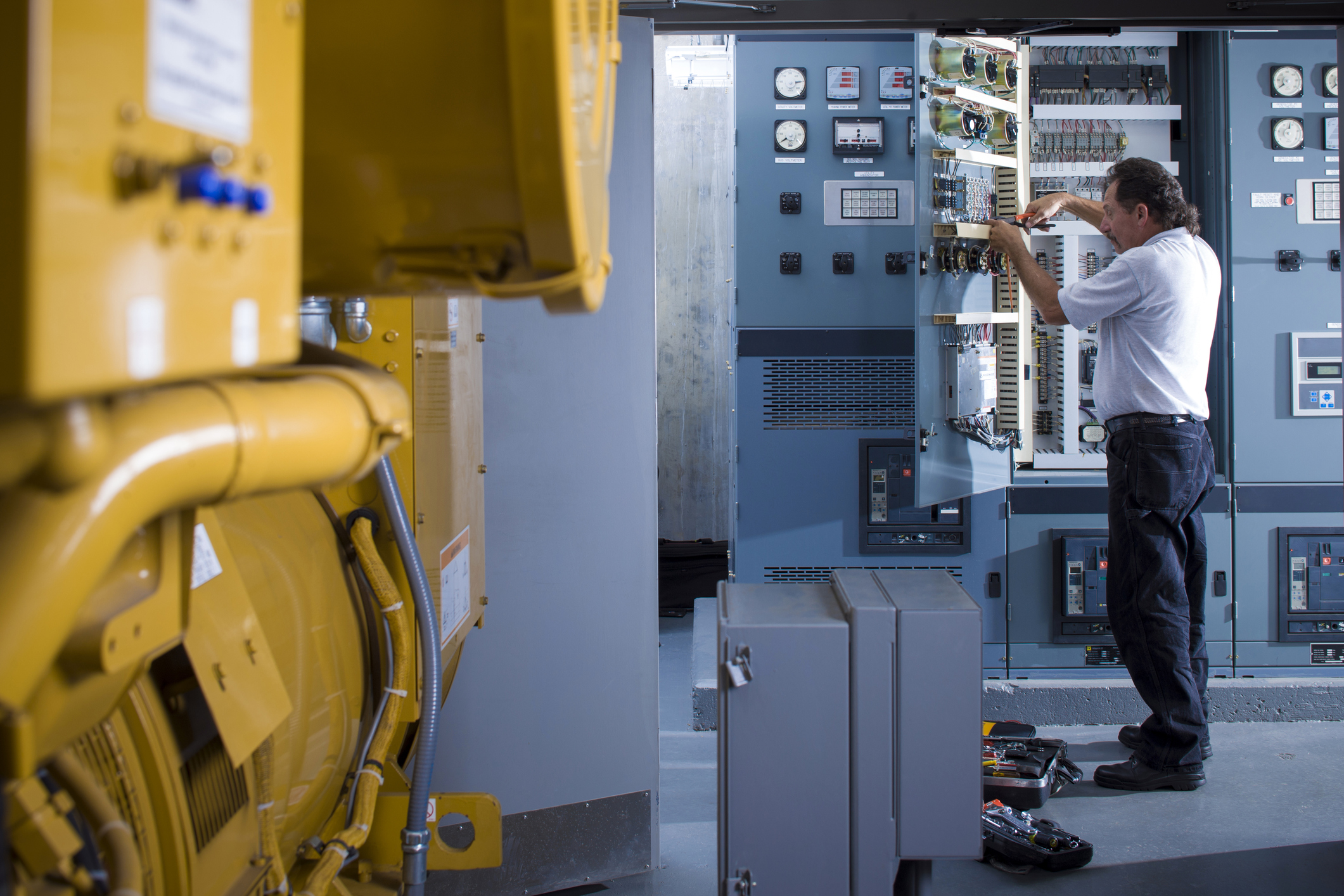 Electrician working on industrial automation control panel inside an equipment room with tools and gauges.