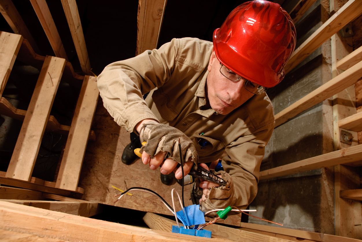 Electrician using wire stripper to cut and crimp electrical wires during residential construction wiring installation.