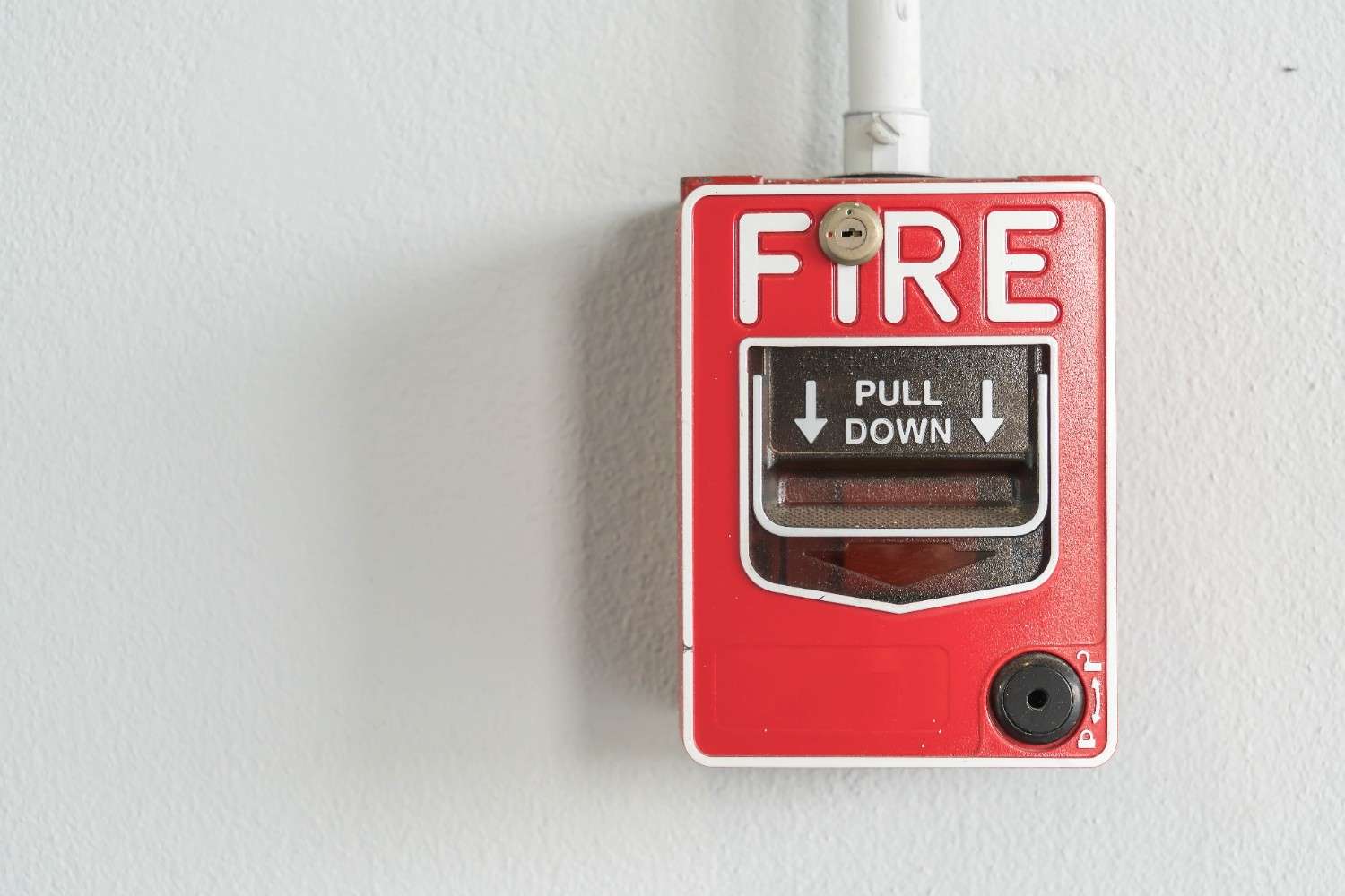 Red emergency fire alarm switch with protective cover mounted on industrial wall – electrical safety device for commercial fire prevention systems.