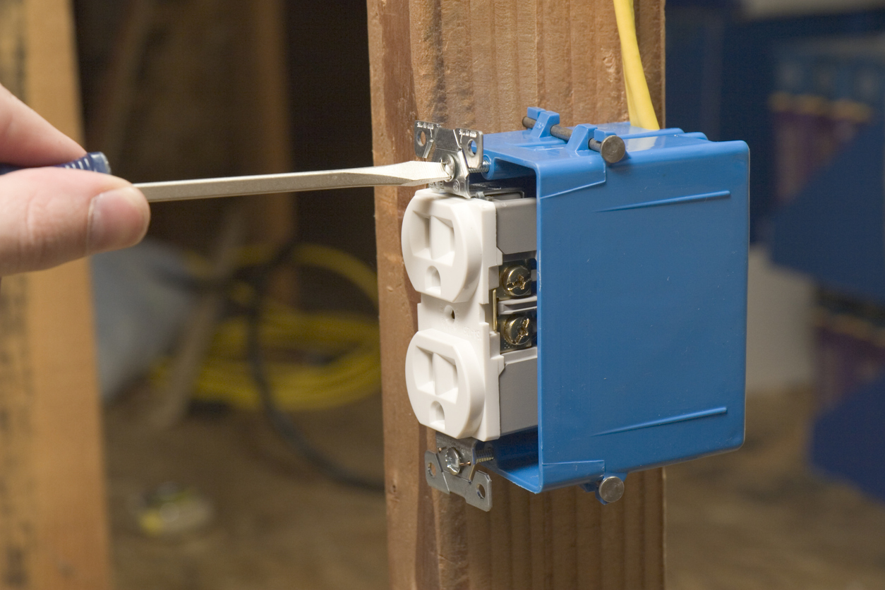 Electrician installing a duplex outlet in a blue PVC electrical box mounted to a wood stud during residential wiring.