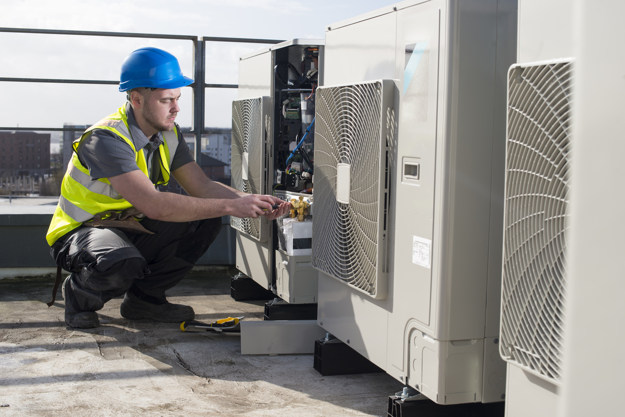 HVAC technician servicing a rooftop smart climate control unit in a commercial building setup.