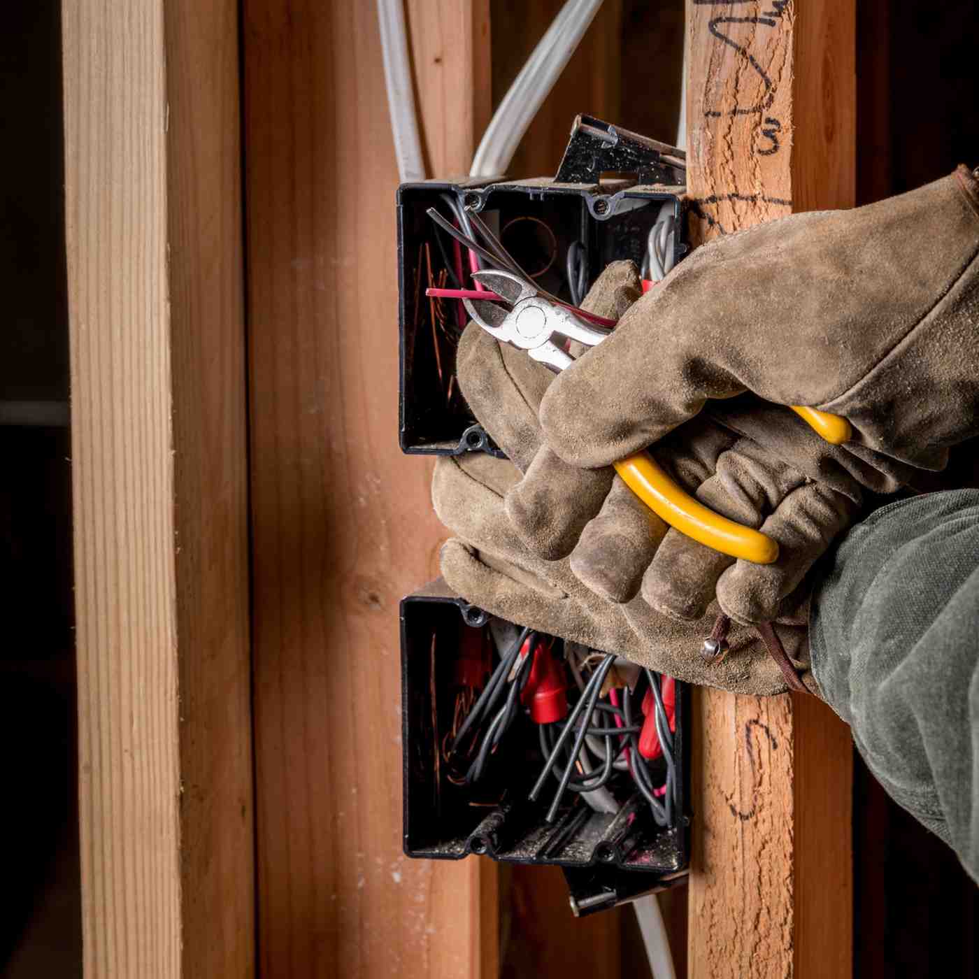 Electrician wiring residential electrical boxes during installation using lineman pliers and insulated gloves