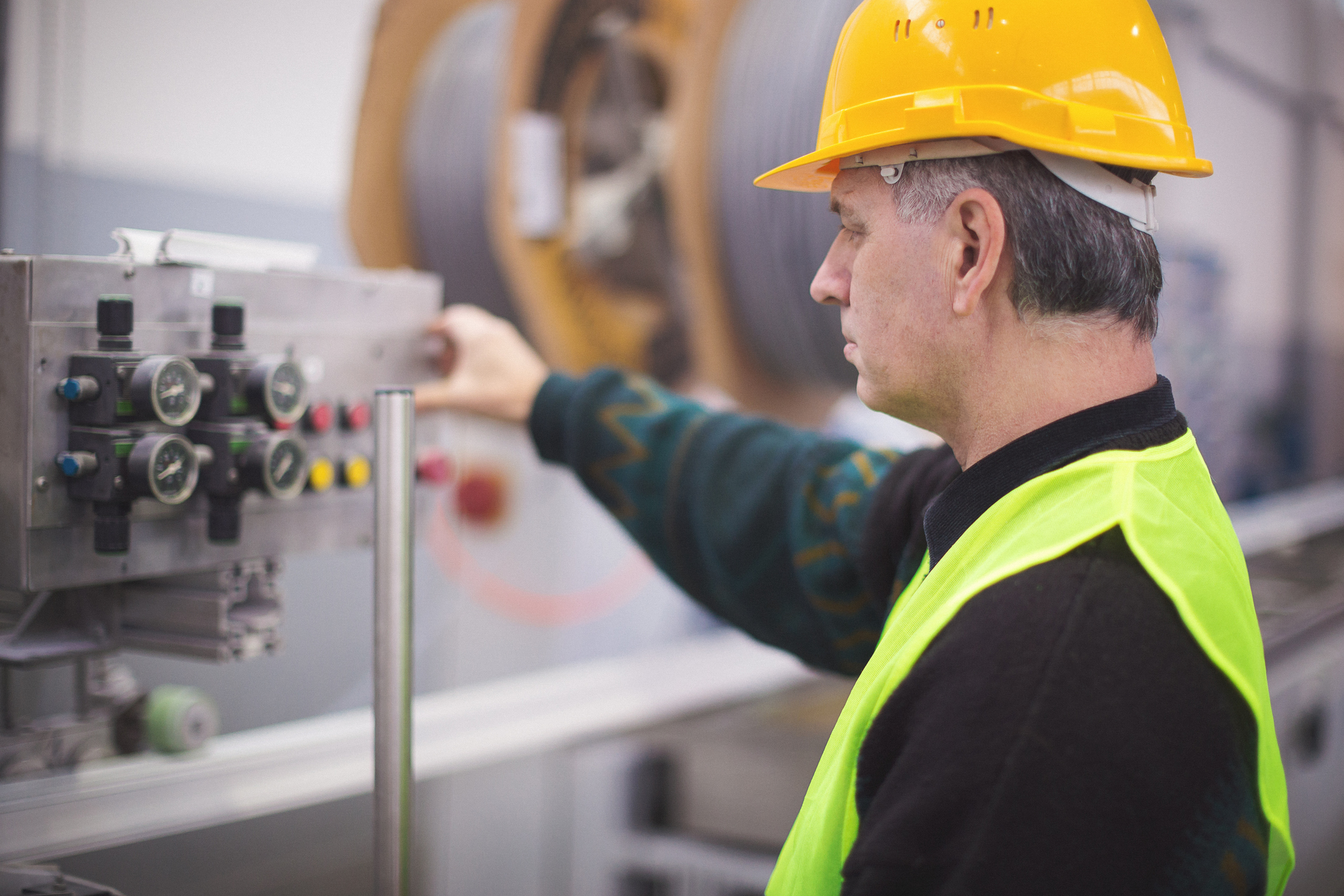 Technician in safety vest and hard hat operating industrial control panel in a manufacturing facility.